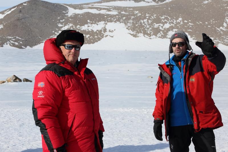 To menn i vinterklede i eit snølandskap. Den eine pekar mot noko bak kamera.